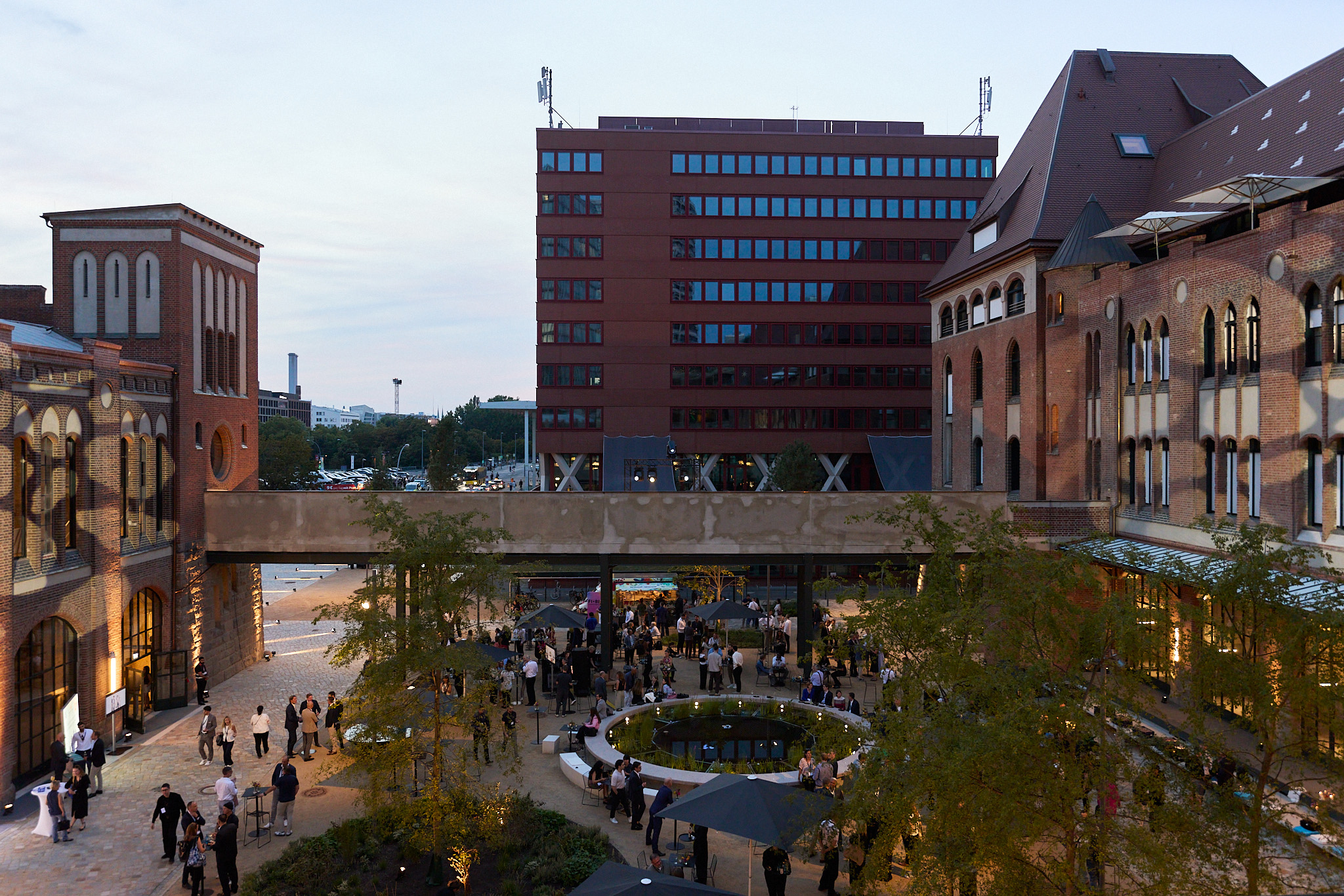 Summer party in the outdoor office at Postbahnhof Berlin with numerous guests surrounded by historic brick buildings.