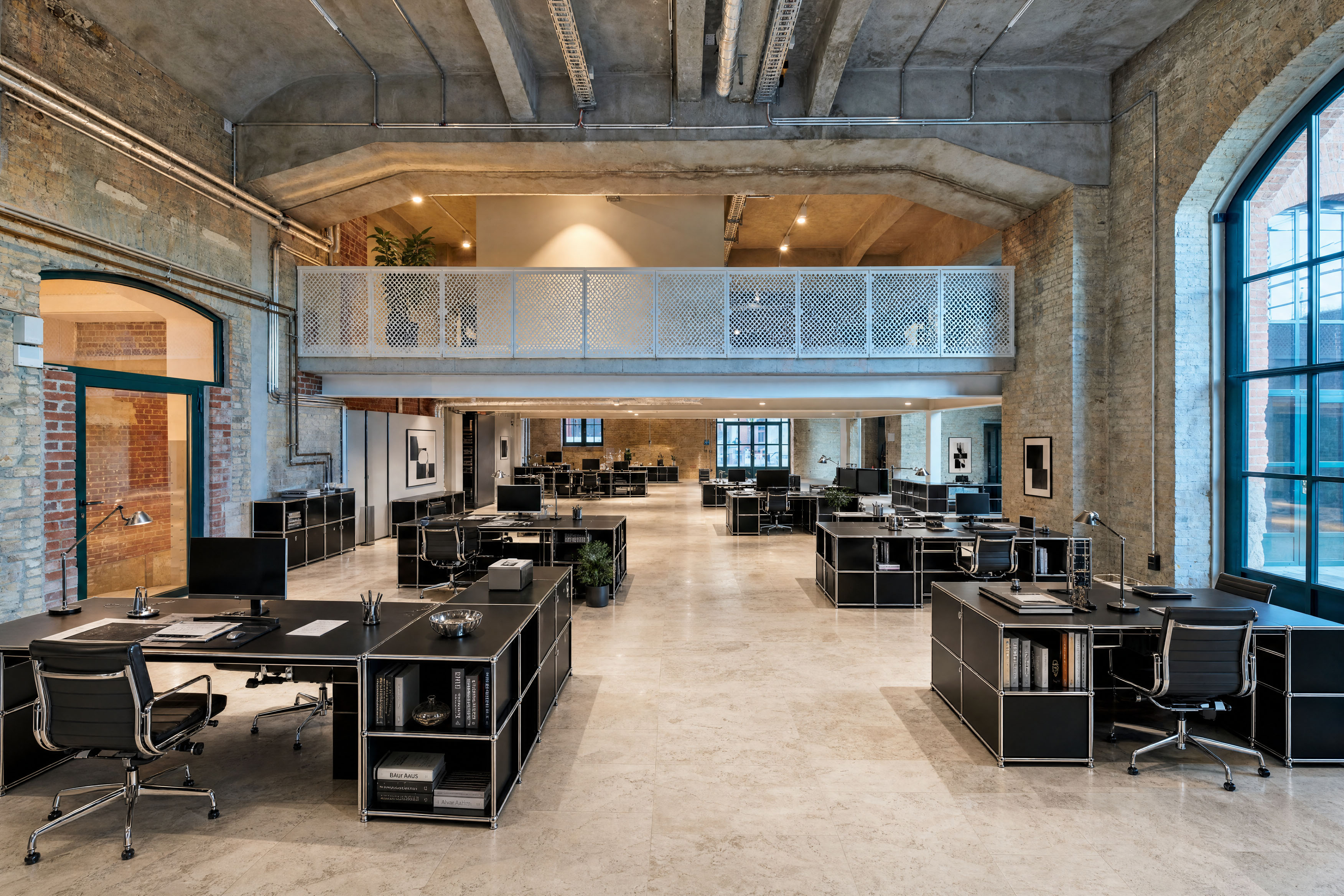 Modern office space at Postbahnhof Berlin with open workstations, historic brick walls, large arched windows and a gallery level.