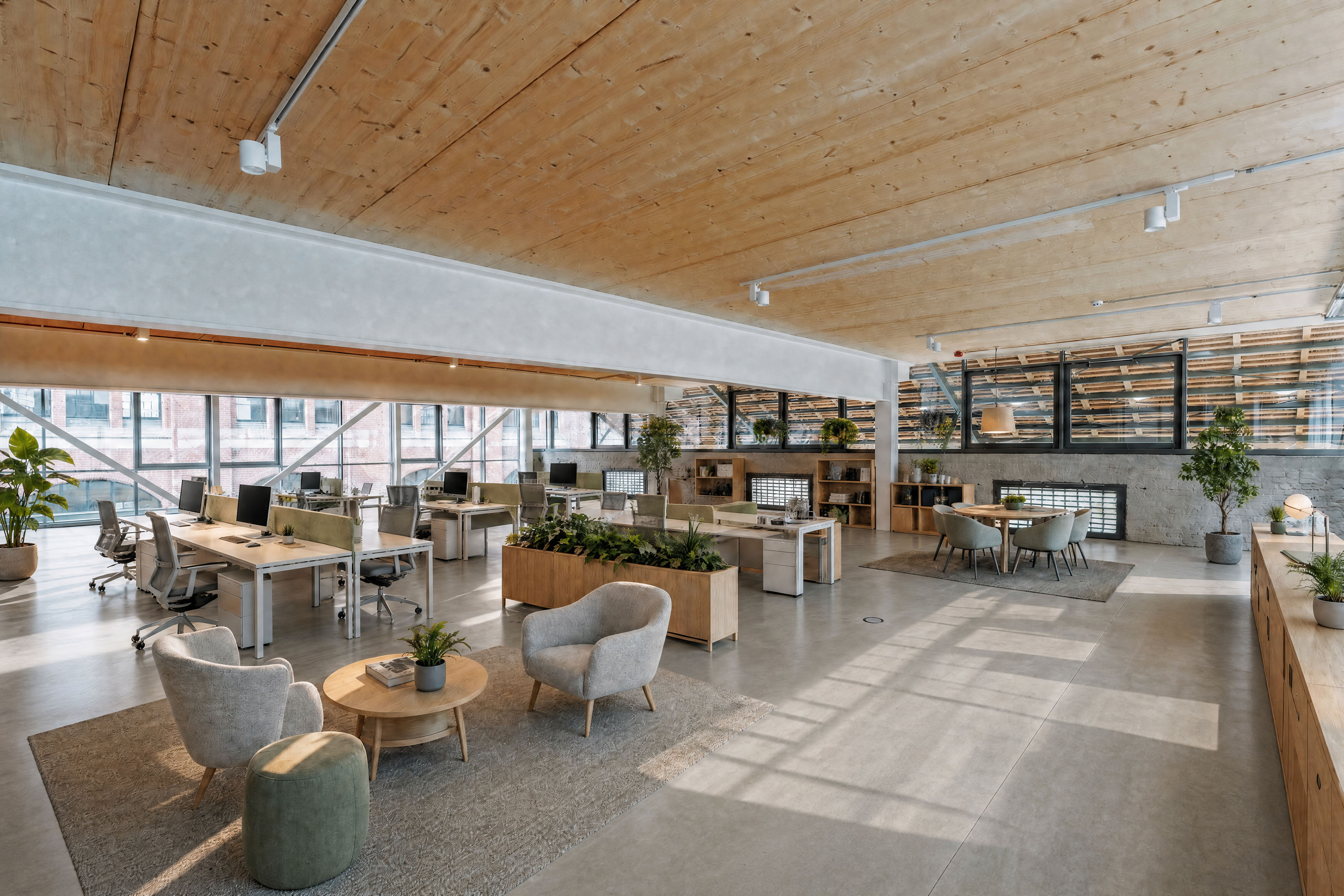Heller, moderner Arbeitsbereich im Postbahnhof Berlin mit offenen Büroarbeitsplätzen, Lounge-Möbeln, Pflanzen und warmer Holzdecke.