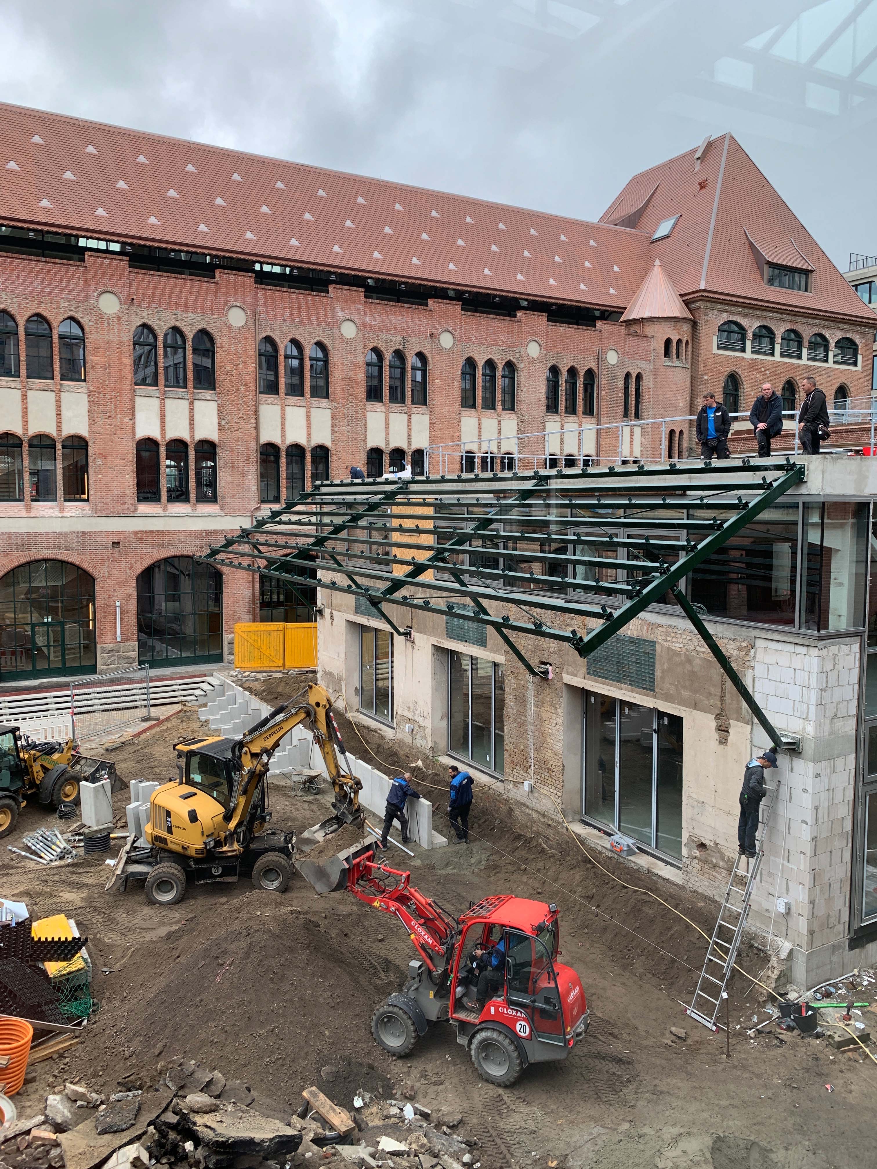 Construction site in front of brick building with construction workers and excavators, view of the emerging structure of the packing room.