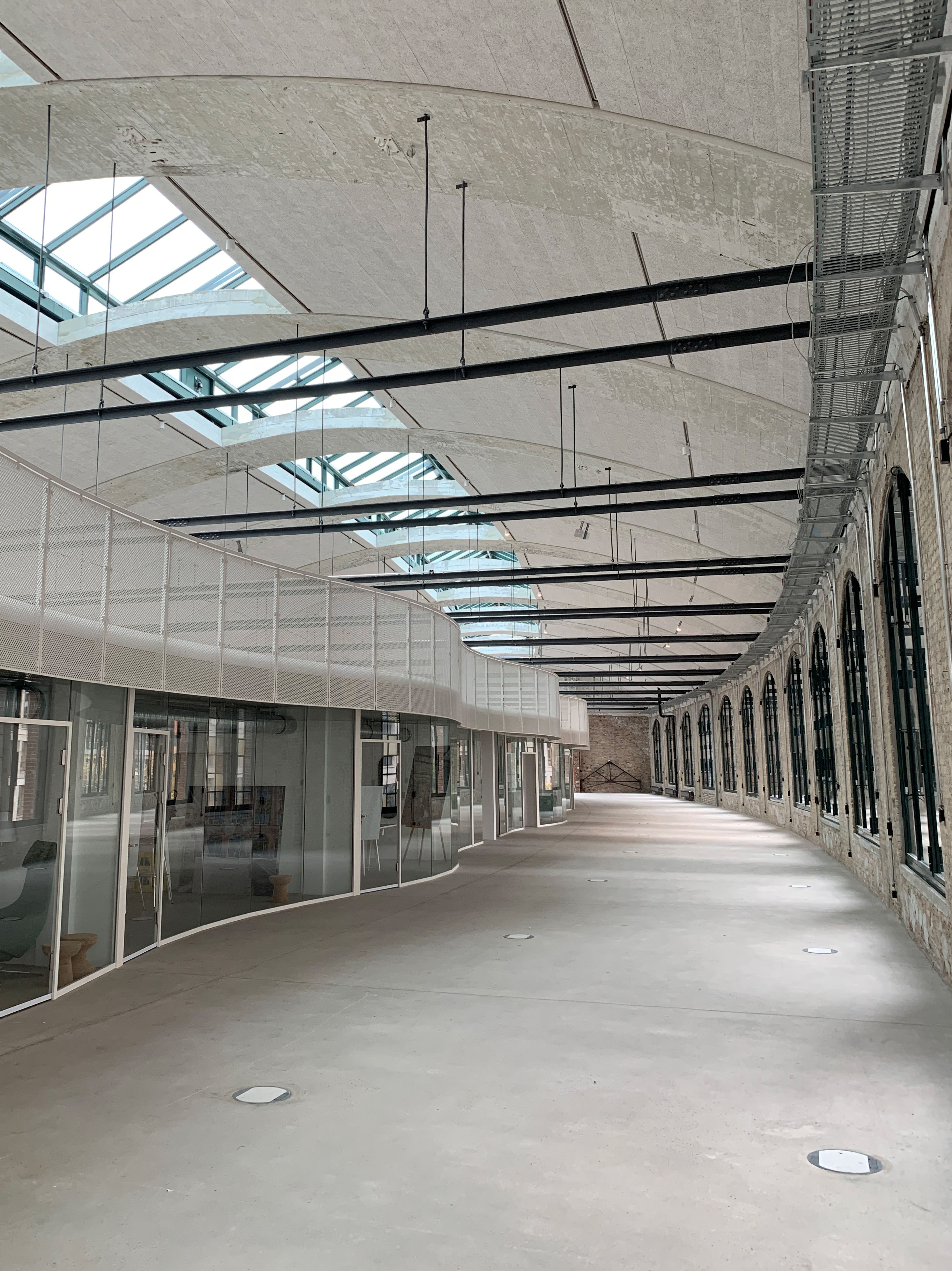 Large, light-filled hallway with glass facades and suspended ceiling, view along the curved architecture.