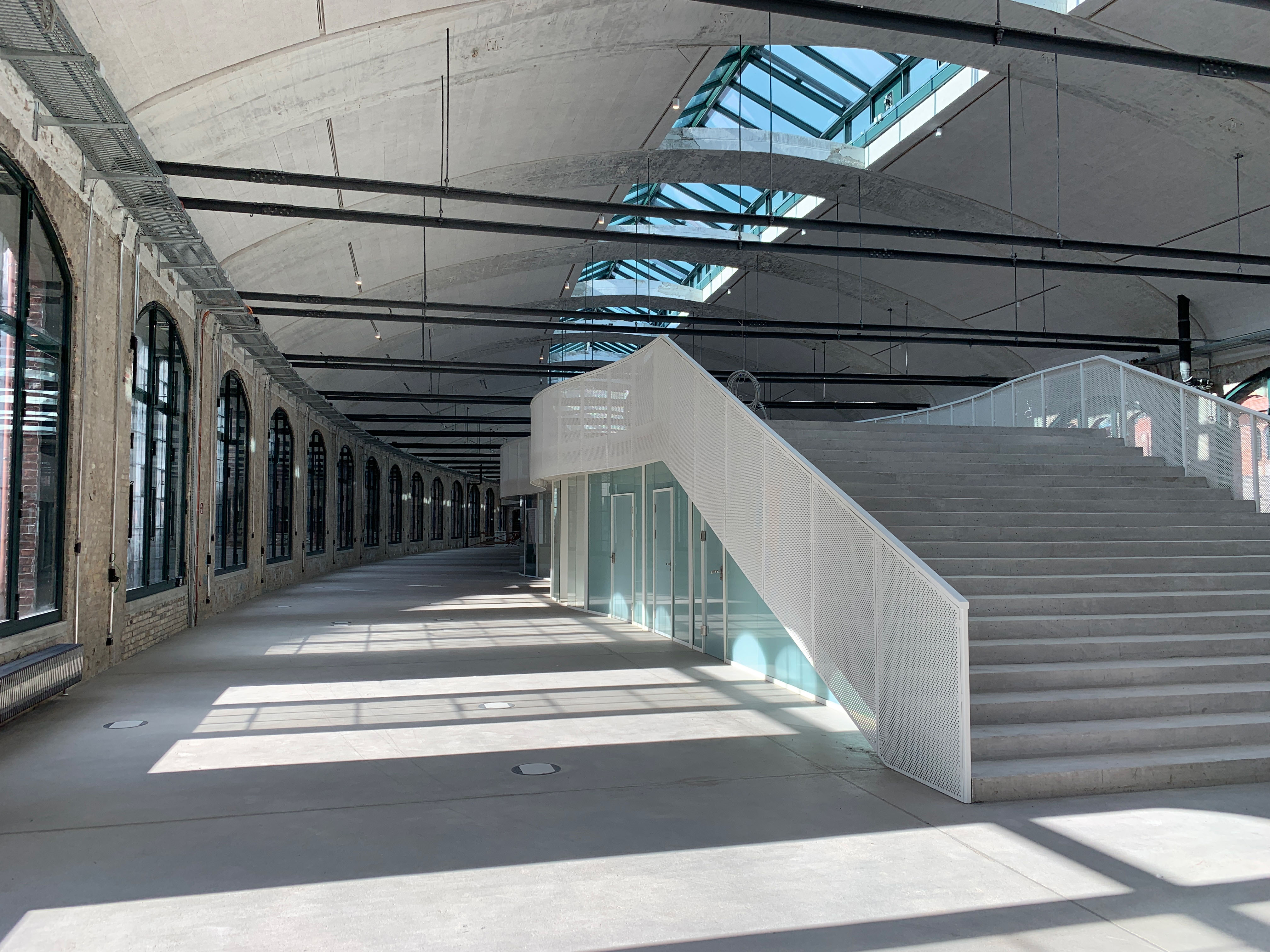 Interior view of the renovated packing room with modern staircase and large windows under an arched structure.
