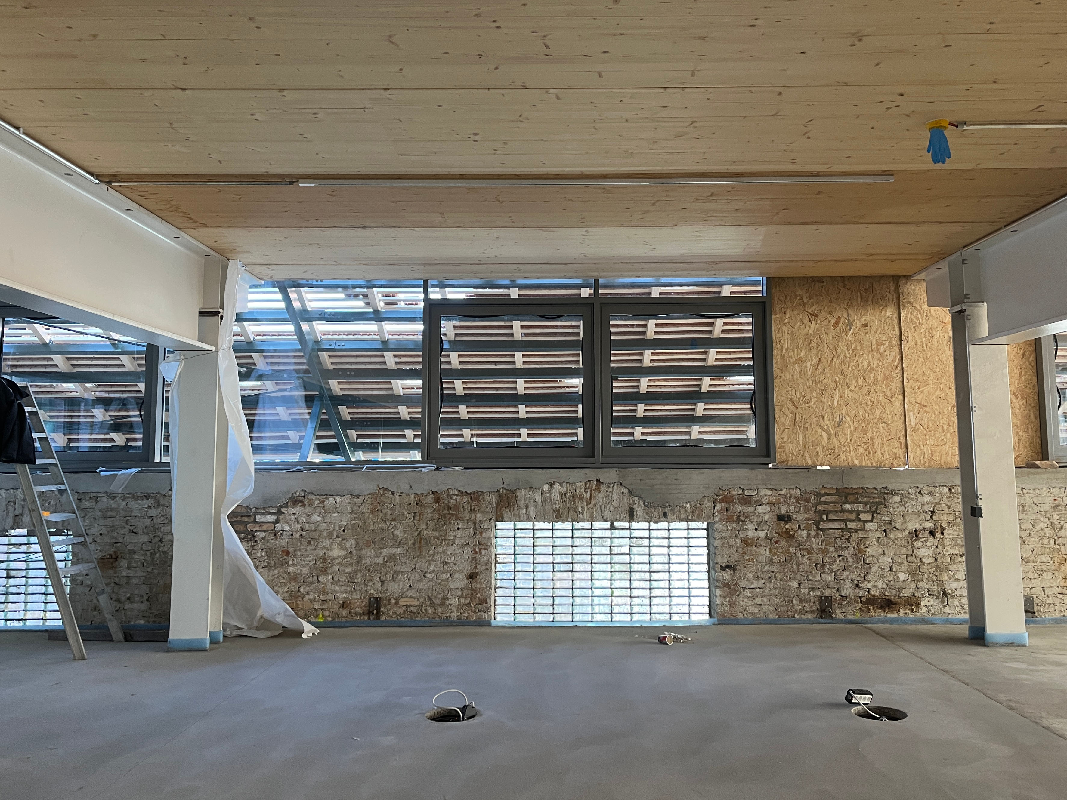 Interior view of construction progress at Postbahnhof Berlin, showing the interior with wooden beam ceiling and exposed brick wall.