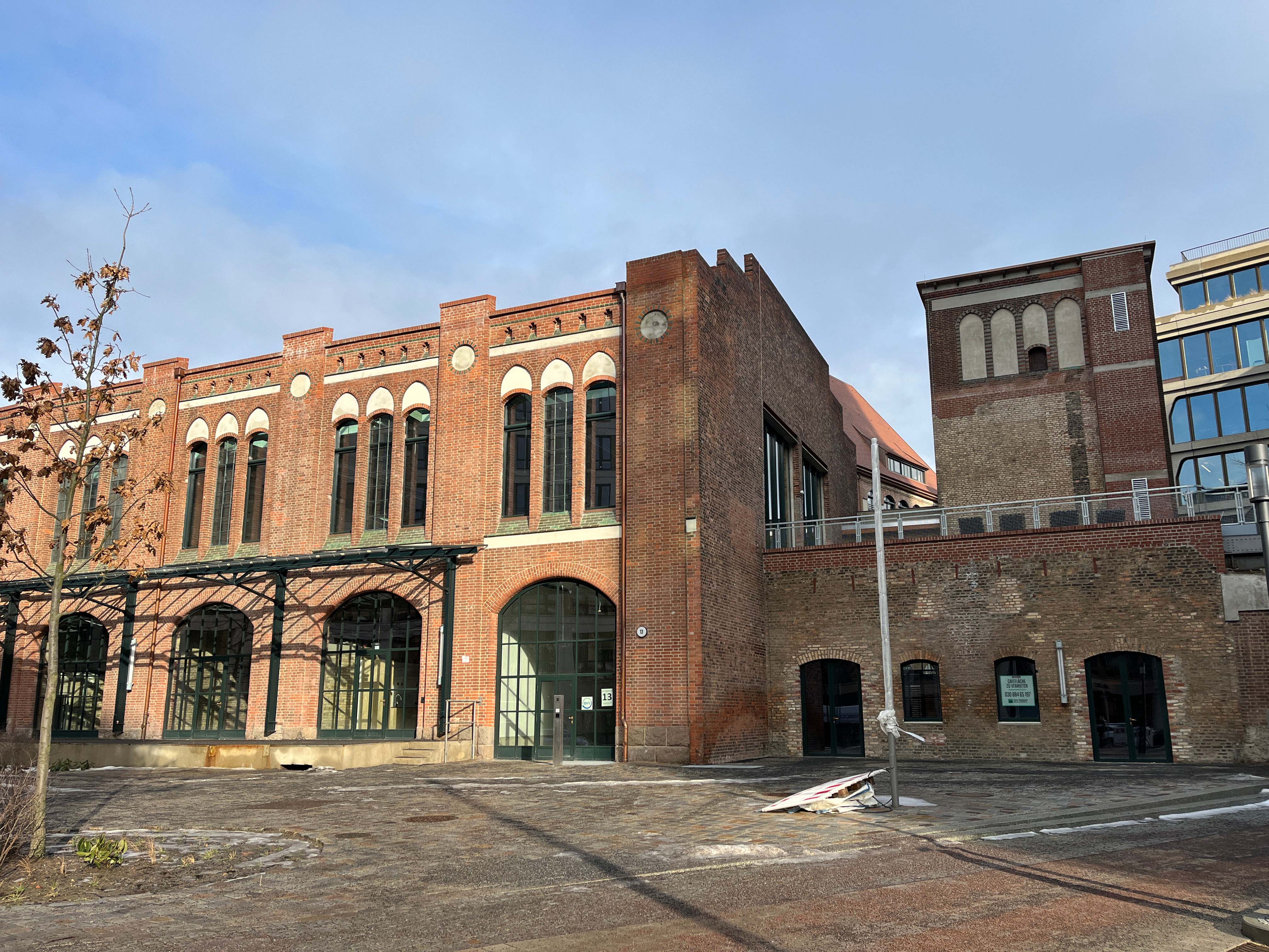 The image shows the construction progress at Postbahnhof Berlin with the exterior view of the café side of the entrance packing hall (EPK) and the refurbished brick façade.