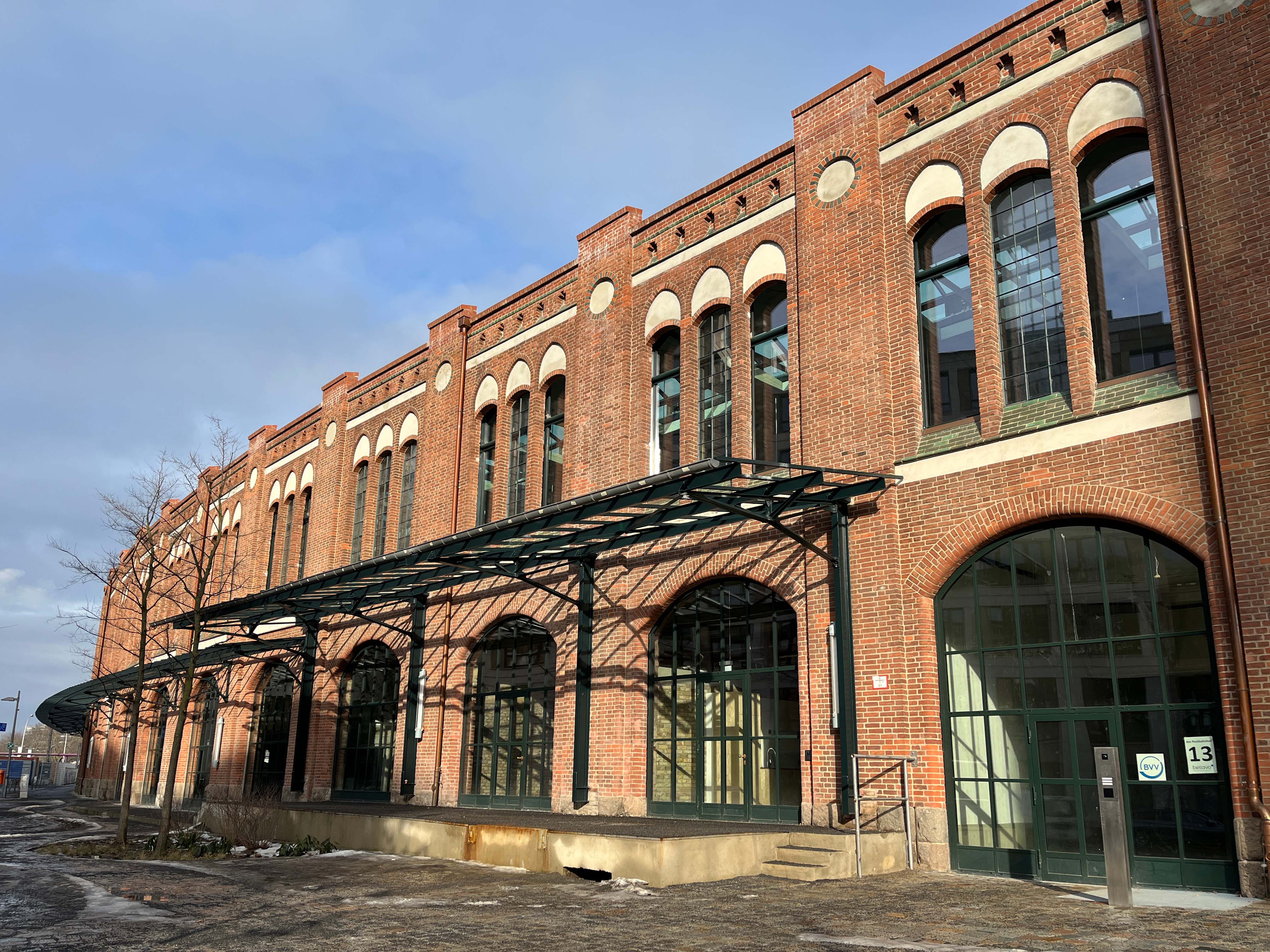 The image shows the construction progress at Postbahnhof Berlin featuring the exterior view of the entrance packing hall (EPK) with its historic brick façade and arched openings.