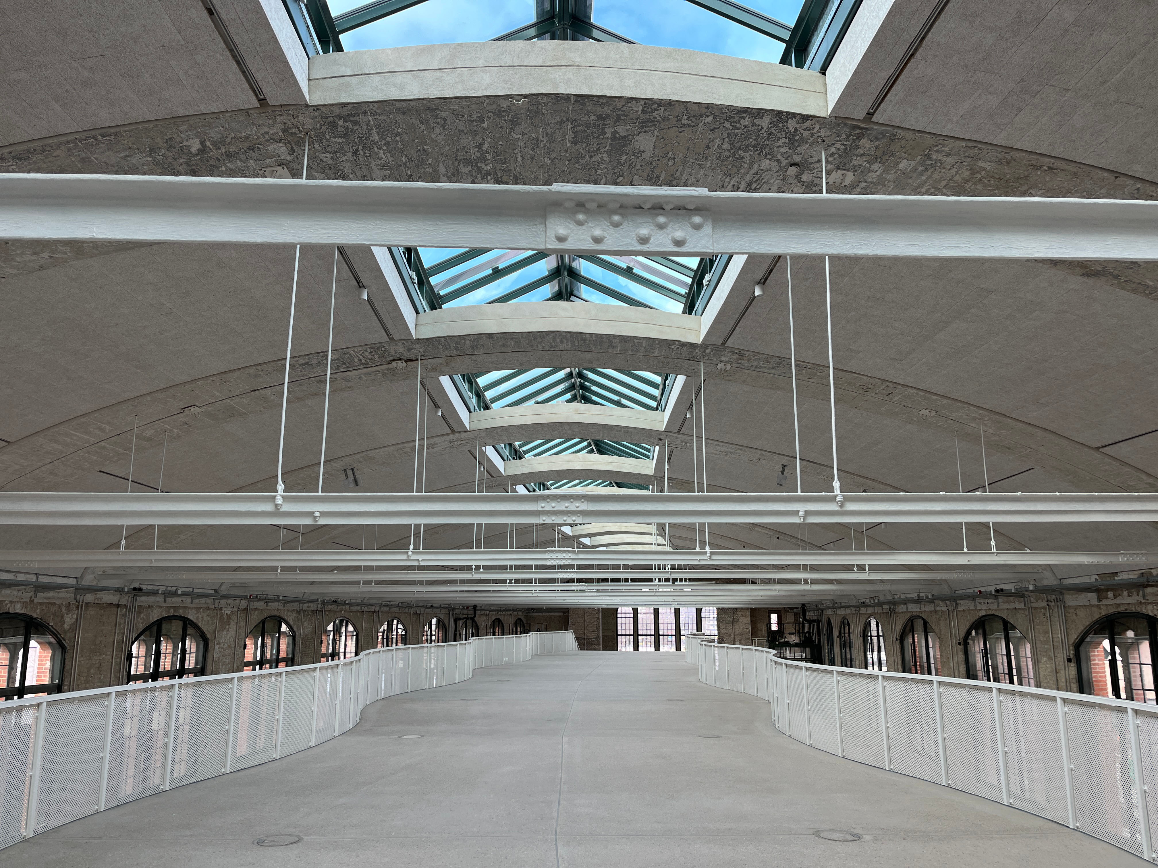 The image shows the construction progress at Postbahnhof Berlin inside the entrance packing hall (EPK) featuring a spacious gallery level, exposed roof trusses and skylights.