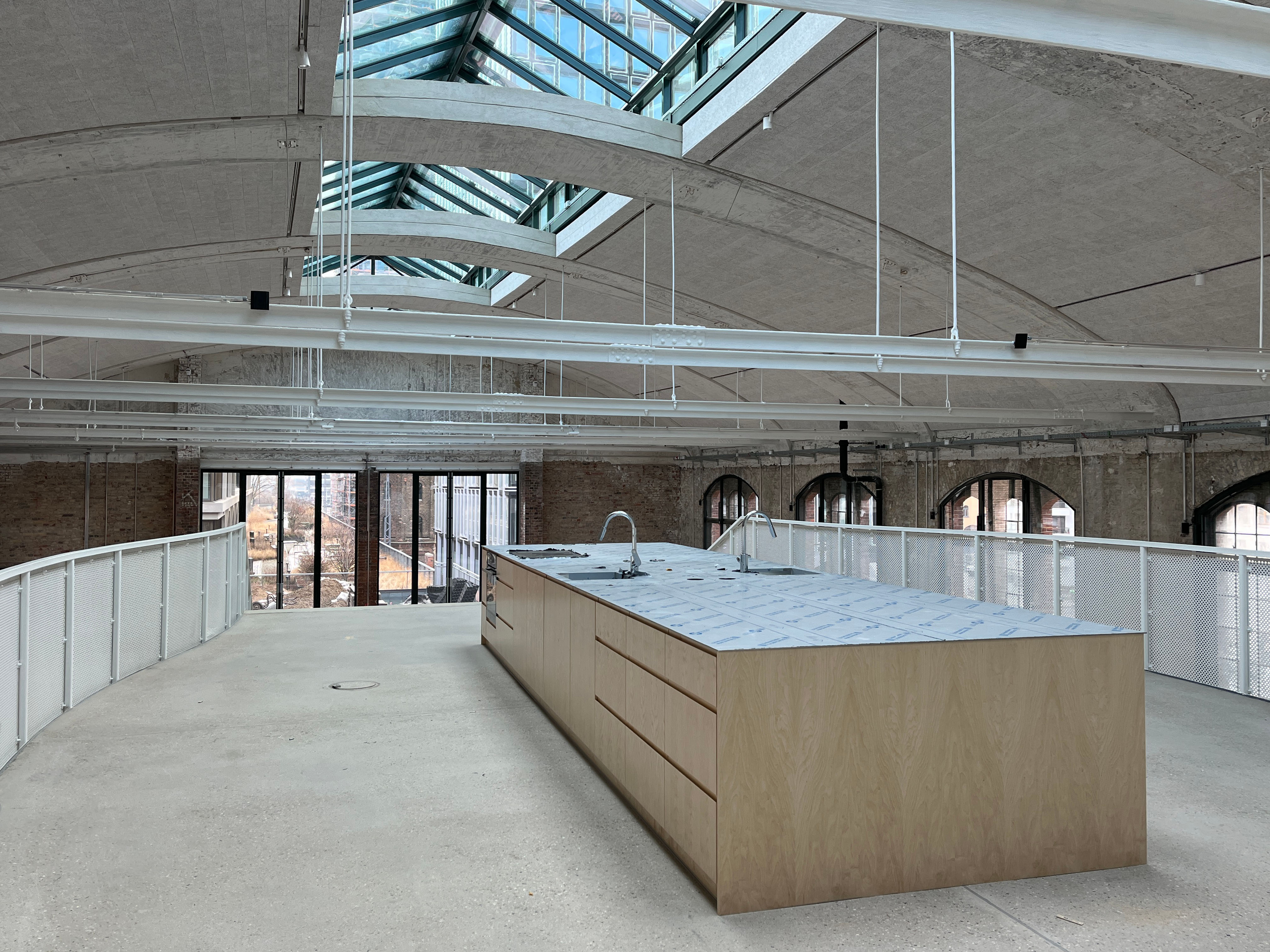 The image shows the construction progress at Postbahnhof Berlin featuring the gallery of the entrance packing hall (EPK) with exposed roof structure and newly installed interior elements.