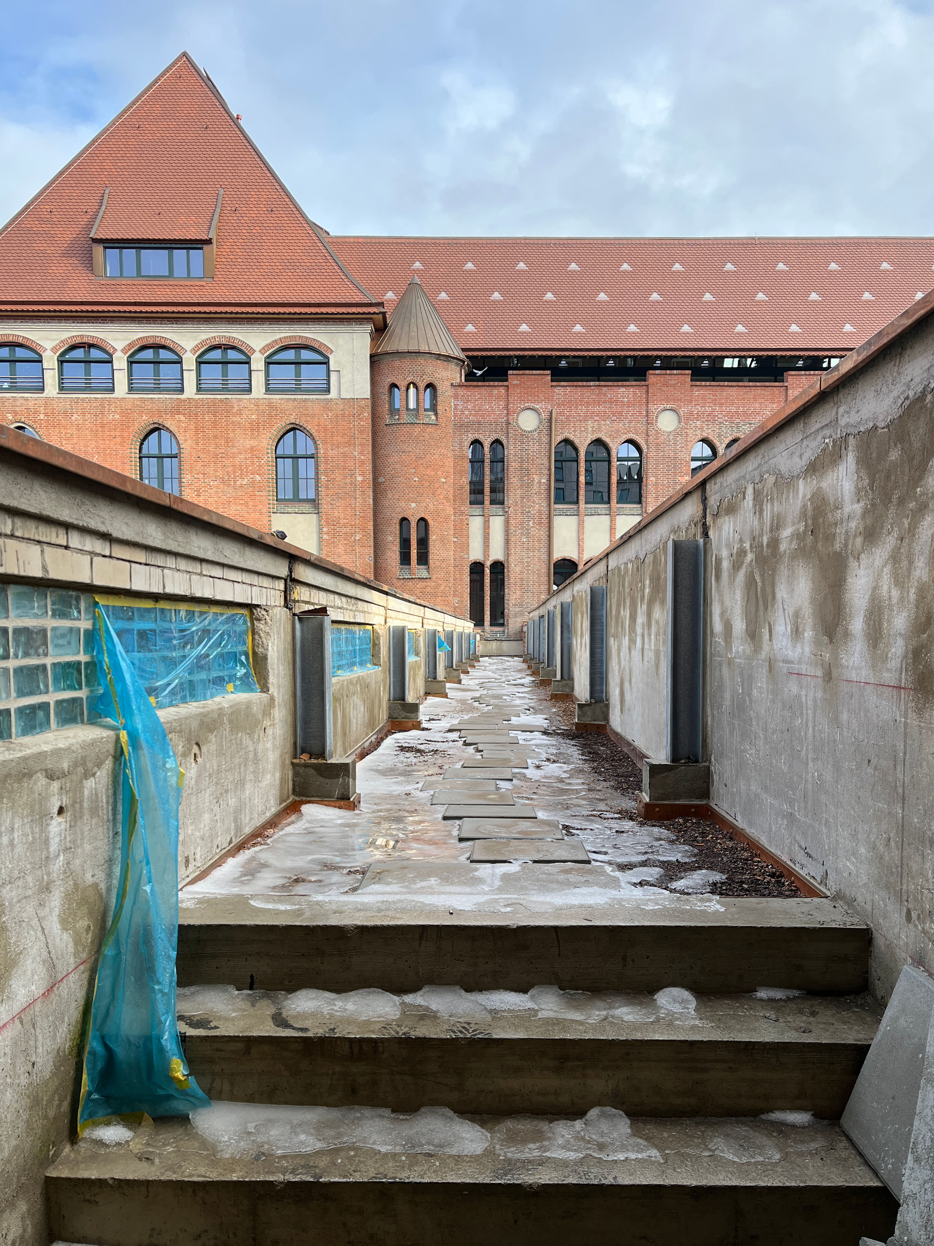 The image shows the construction progress at Postbahnhof Berlin featuring the parcel belt terrace in the exterior area with a view of the historic brick architecture.
