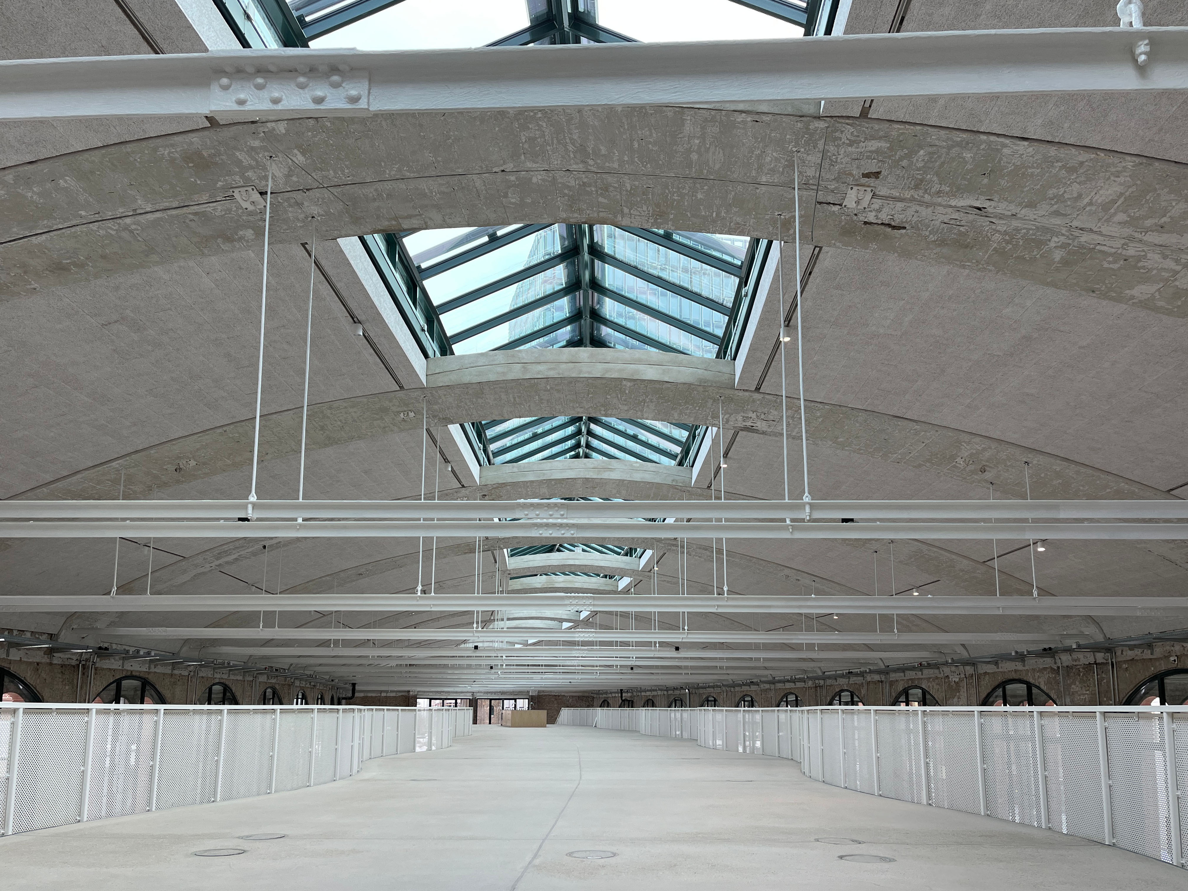 The image shows the construction progress at Postbahnhof Berlin featuring the spacious gallery level of the entrance packing hall with central roof skylights.
