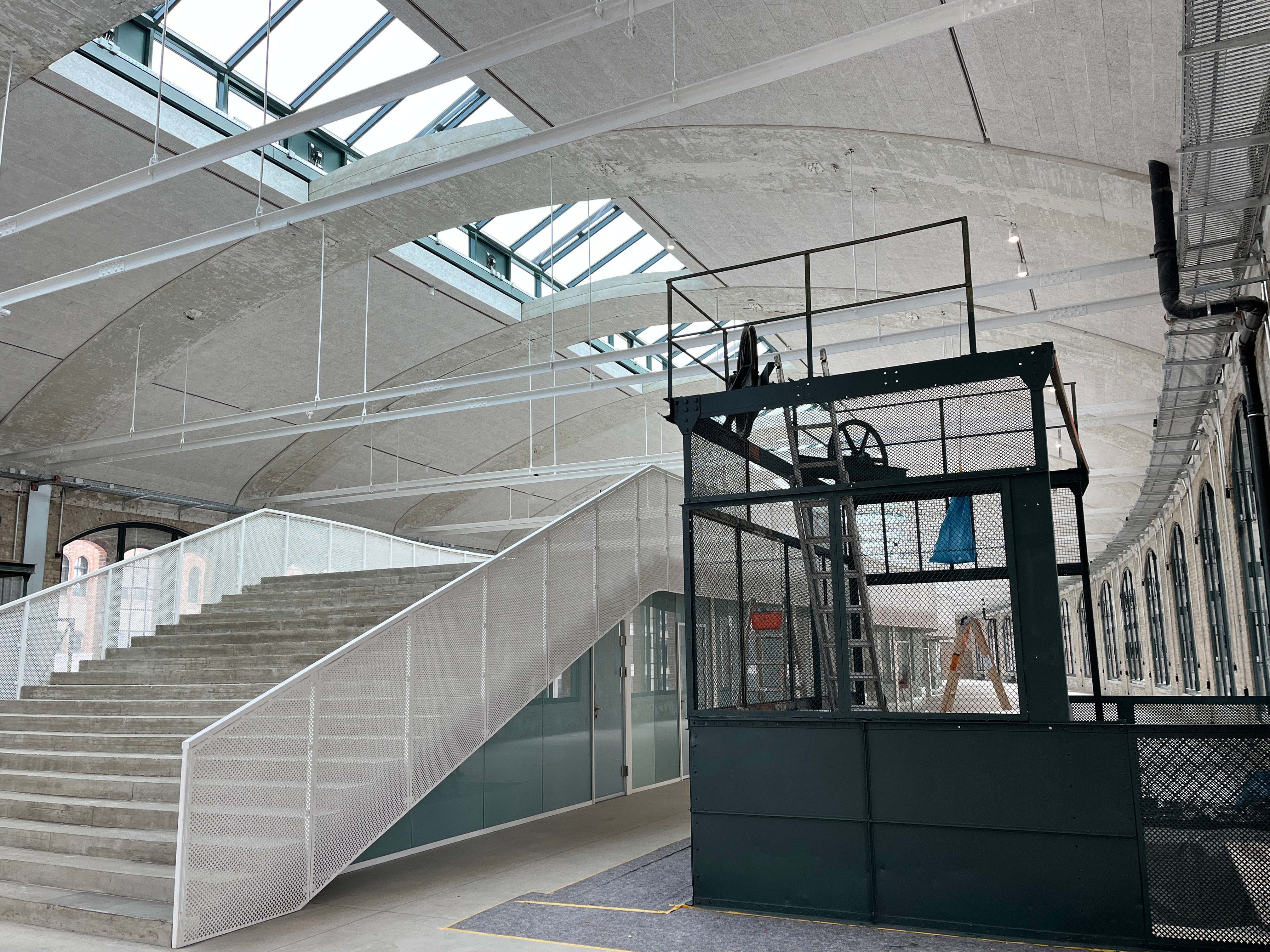 The image shows the construction progress at Postbahnhof Berlin inside the entrance packing hall featuring the gallery, stair structure and skylights.