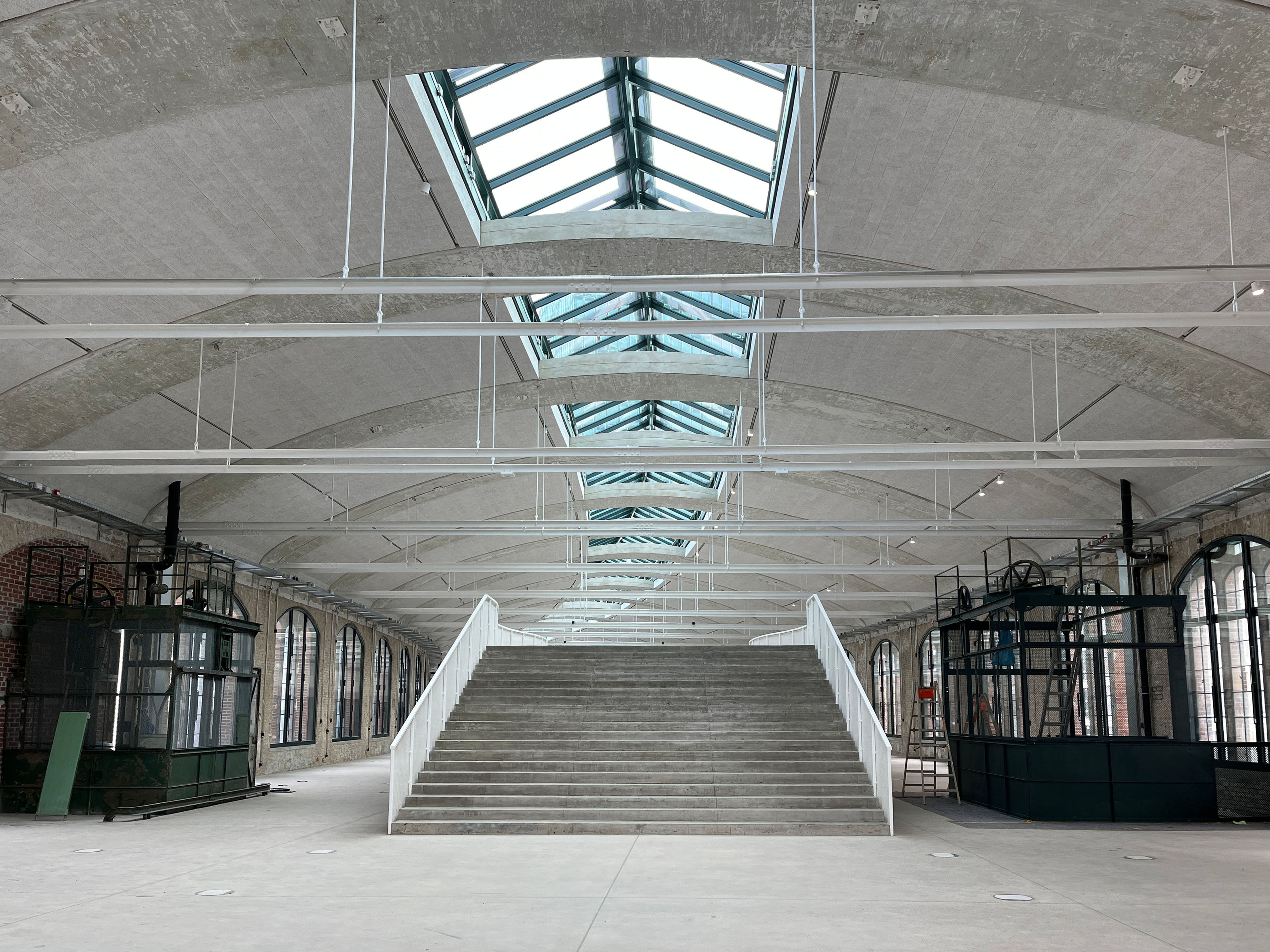 The image shows the construction progress at Postbahnhof Berlin featuring the central interior of the entrance packing hall with staircase and large skylights.